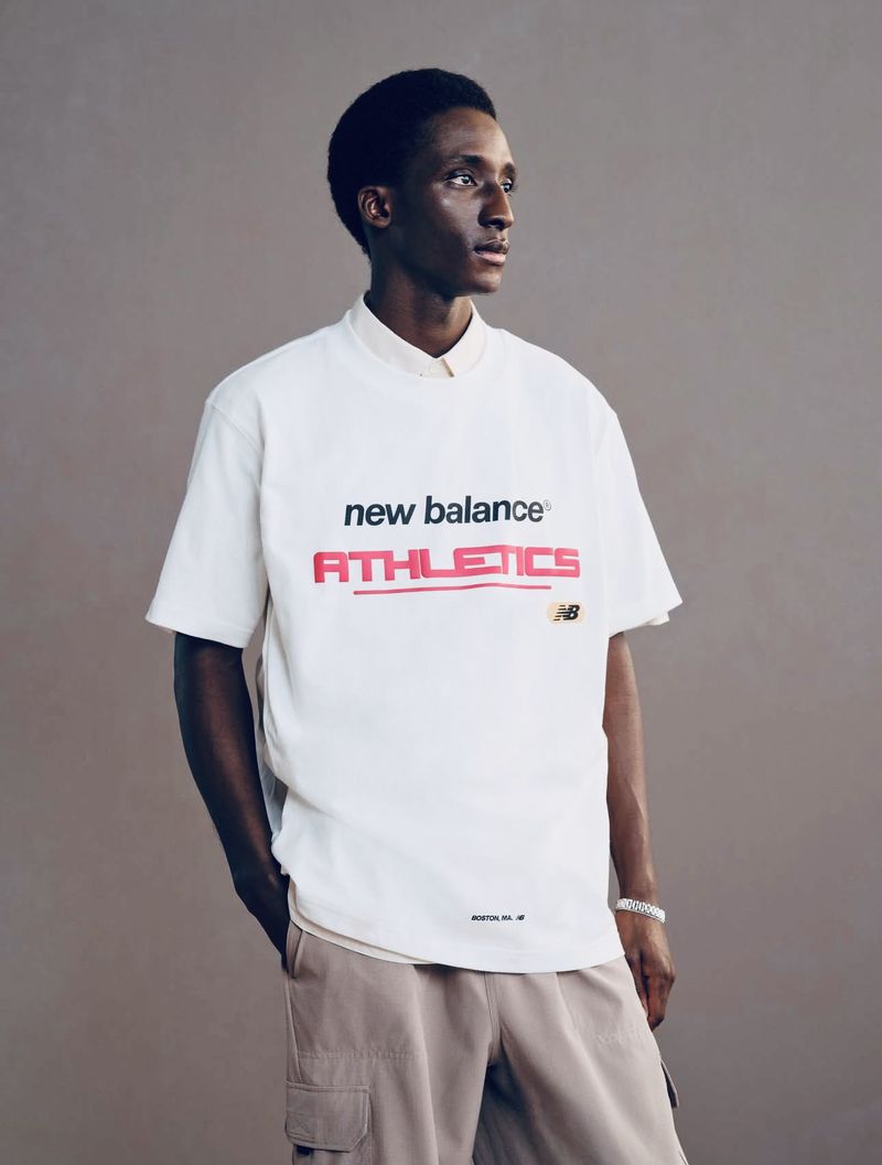 Portrait of a Black man wearing a white New Balance t-shirt and beige cargo pants against a grey background in a studio setting.