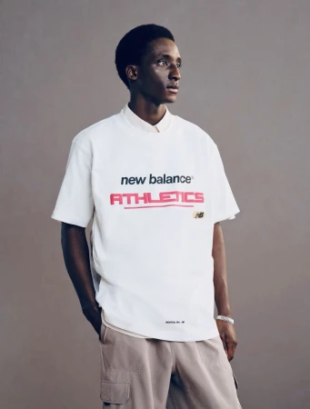 Model Mamadou Diagne wearing a white New Balance Athletics t-shirt and beige cargo pants against a neutral grey studio background.