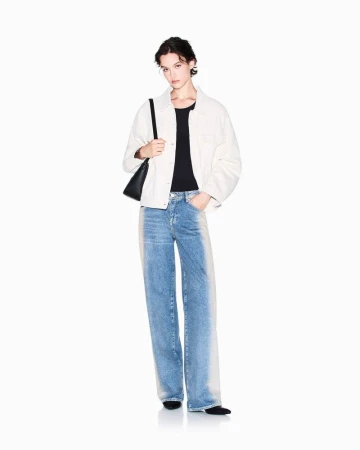 A full-length studio shot of a young adult woman in jeans, a black top, and a jacket, standing in front of a clean white backdrop.