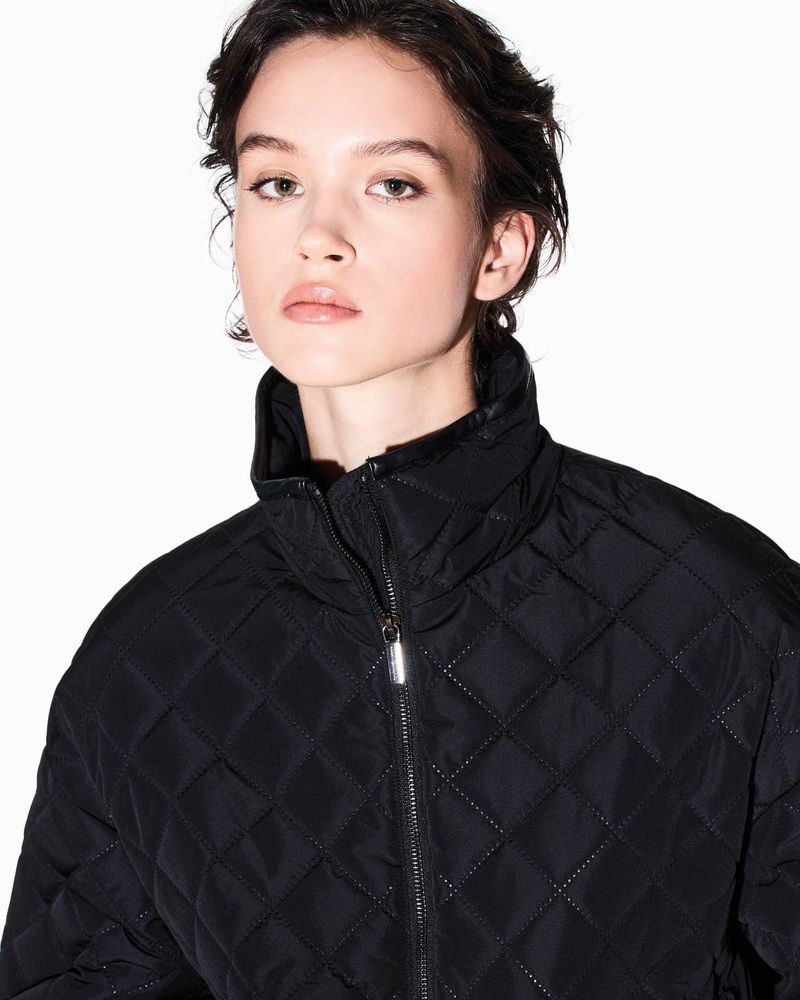 Close-up of a young woman wearing a black quilted jacket against a white background in a fashion portrait. Beauty shot.