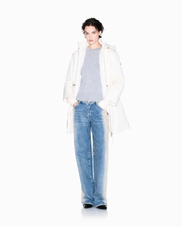 Model wearing an oversized white parka, grey sweater, and faded blue jeans standing against a solid white studio background.