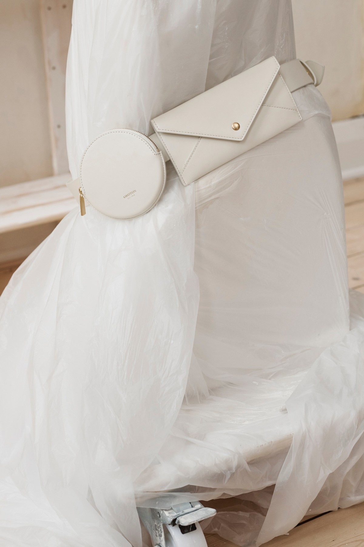 Cream-colored leather envelope-shaped wallet with a gold snap, along with a small round coin purse on plastic-wrapped furniture.