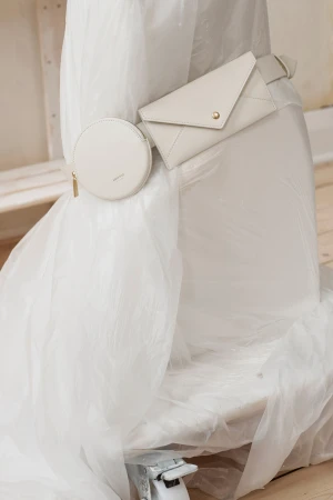 Cream-colored leather envelope-shaped wallet with a gold snap, along with a small round coin purse on plastic-wrapped furniture.