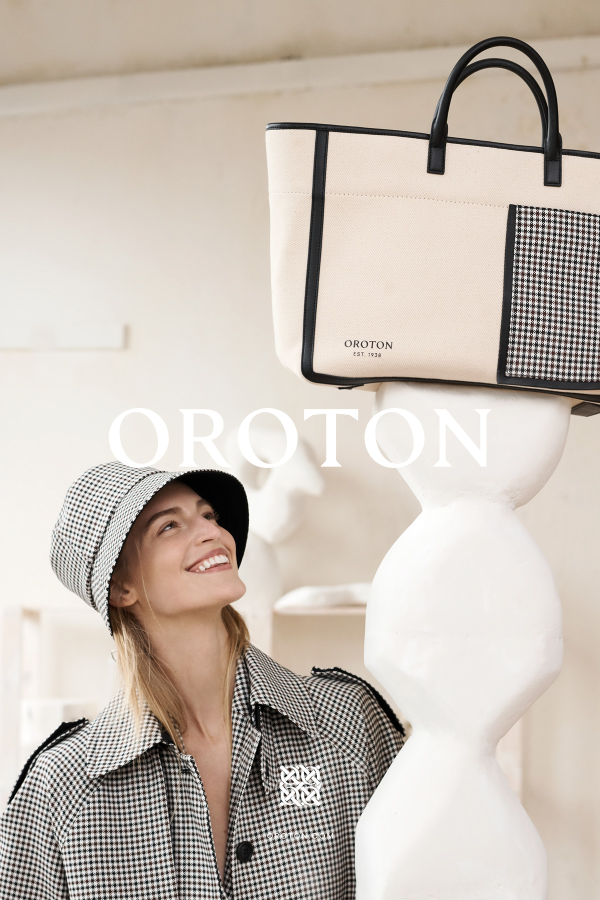 Fashion editorial featuring a model in a patterned jacket and bucket hat, posing near a handbag, with a neutral background.