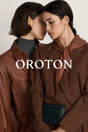 Two adult women pose in a fashion shot, showcasing brown jackets in an indoor setting with the brand name Oroton displayed.