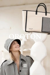 Woman in houndstooth bucket hat and coat smiling up at a cream and black canvas tote bag on a pedestal