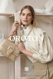 Model Vanessa Axente holding a beige Oroton handbag while posing next to a light wooden shelving unit in an autumn winter campaign