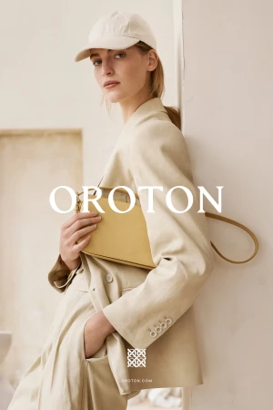 Model in cream blazer and baseball cap holding yellow leather handbag against a neutral wall