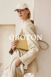 Model in cream blazer and baseball cap holding yellow leather handbag against a neutral wall