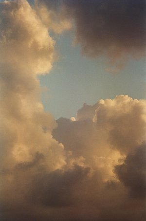 Dramatic clouds fill the frame with warm light and soft edges, framing a glimpse of the pale blue sky in a vertical composition.