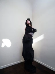Lady Gaga wearing a hooded black dress standing in a corner with white walls for Elle U.S. February 2025 Cover