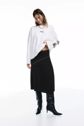 Model in a white long-sleeve top and black midi skirt posing against a seamless white background for Pull and Bear.