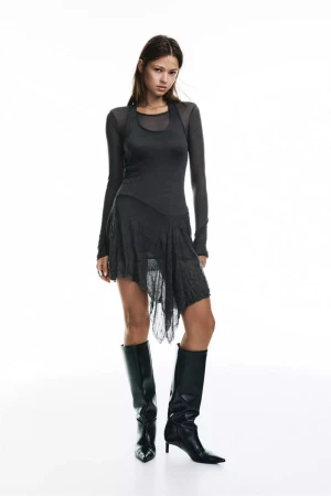 Model Didi Sviridova poses in a black layered asymmetrical dress and black knee-high leather boots against a white studio background.