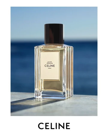 Celine fragrance bottle against a blurred blue background. The bottle features clear glass and a black cap on a concrete surface.