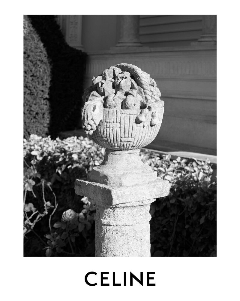 Monochrome photograph of a stone garden ornament on a pillar, with plants in the background and the text "CELINE" below the image.