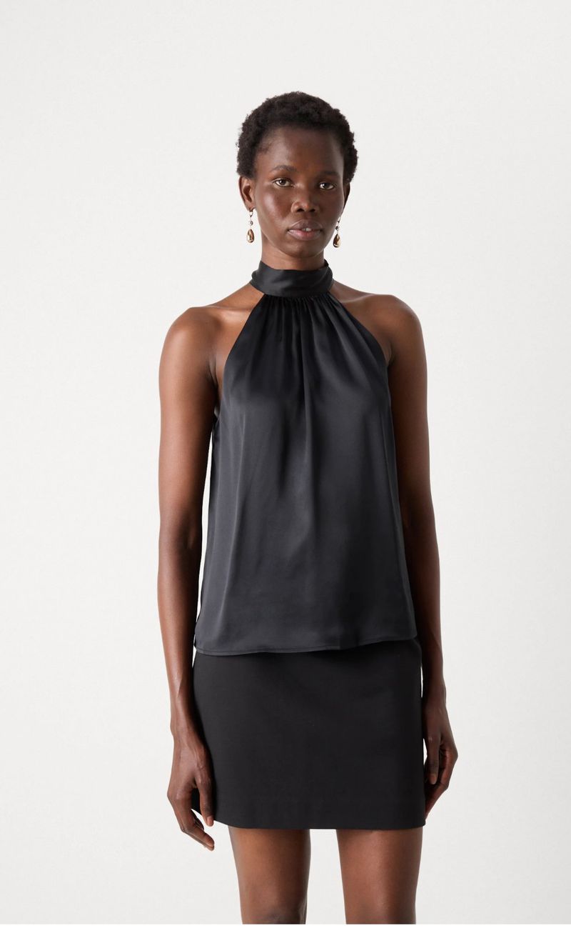 Adult female with dark skin poses in a sleeveless black top and matching mini skirt in a studio setting. Fashion shot, neutral expression.