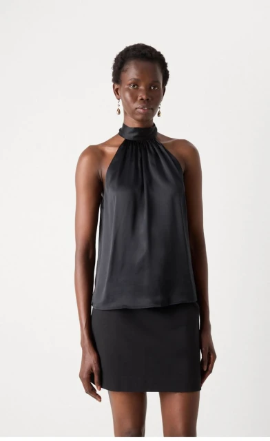 Adult female with dark skin poses in a sleeveless black top and matching mini skirt in a studio setting. Fashion shot, neutral expression.