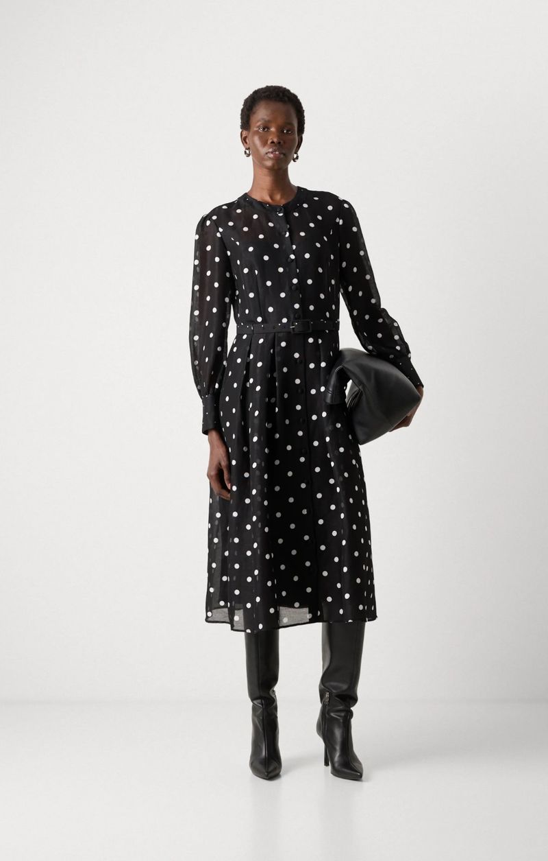 Elegant Black Dress: A model showcases a long-sleeved, polka-dot midi dress, paired with sleek black boots and a matching handbag against a white backdrop.