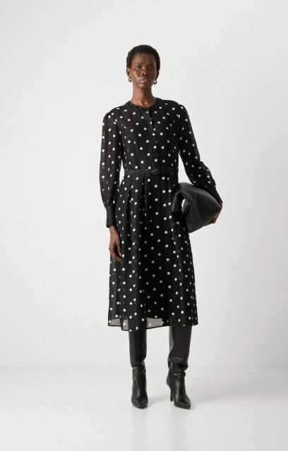 Elegant Black Dress: A model showcases a long-sleeved, polka-dot midi dress, paired with sleek black boots and a matching handbag against a white backdrop.