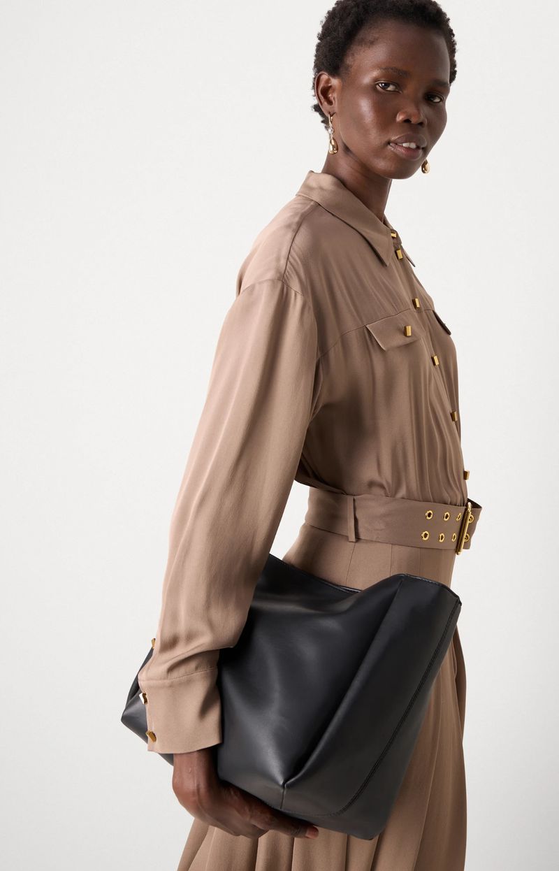 Stylish African woman in brown shirt dress with black tote bag. Fashion editorial shot in a bright studio setting. Neutral fashion.