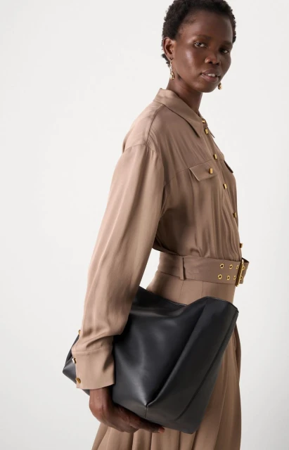 Stylish African woman in brown shirt dress with black tote bag. Fashion editorial shot in a bright studio setting. Neutral fashion.