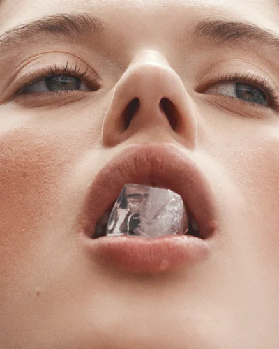 Extreme close-up portrait of a woman holding a single ice cube between her lips shot from below by photographer Tim Ashton.