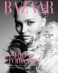 Close-up black and white portrait of Lily-Rose Depp wearing a feathery textured garment against a plain grey backdrop.