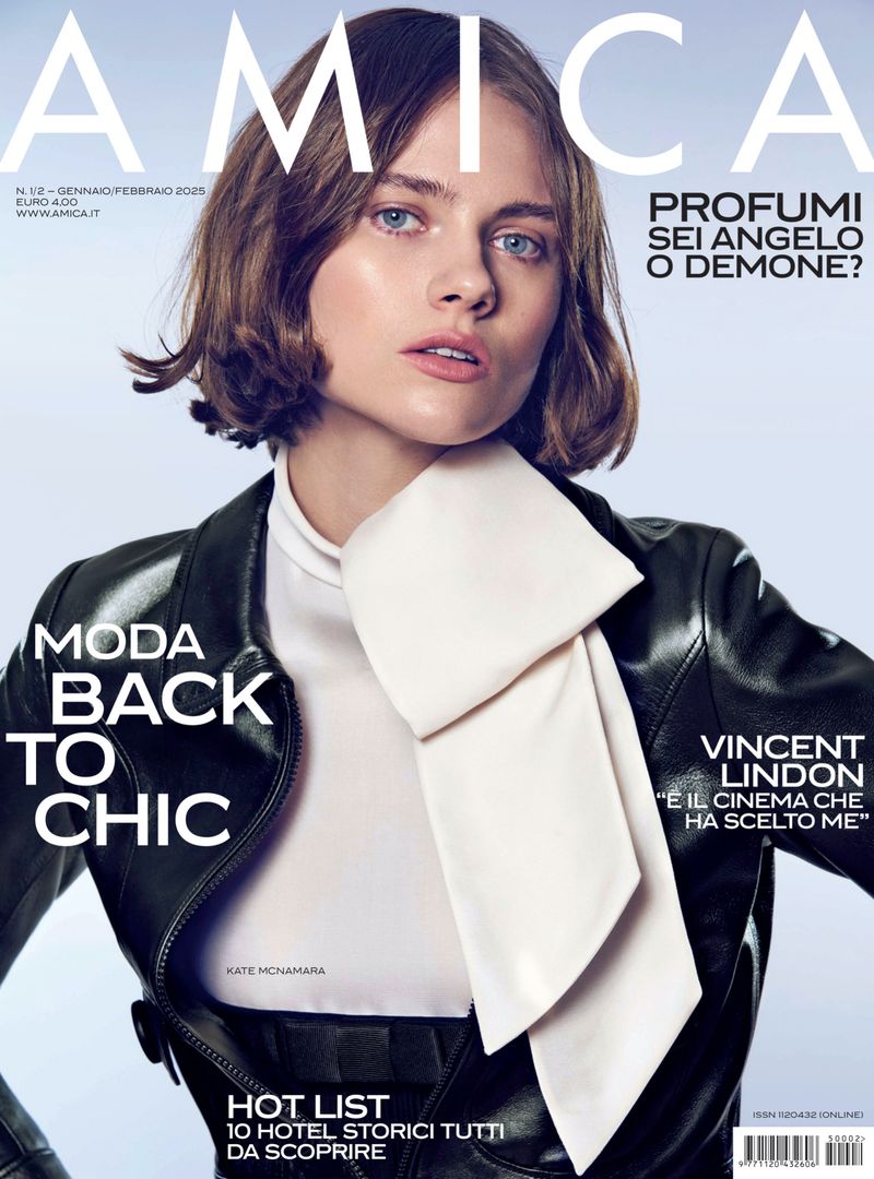 Amica magazine cover features a portrait of a brunette woman wearing a black leather jacket and a white top, with a soft blue background.