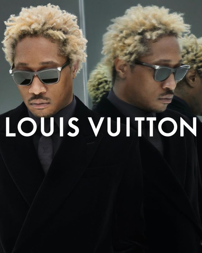 Portrait of a Black man with blonde hair wearing sunglasses and a black suit, next to a blurred reflection; Louis Vuitton logo is visible.