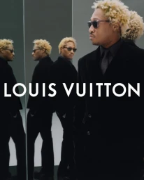 Future in a black suit with sunglasses standing against a reflective mirrored grey wall in a Louis Vuitton campaign.