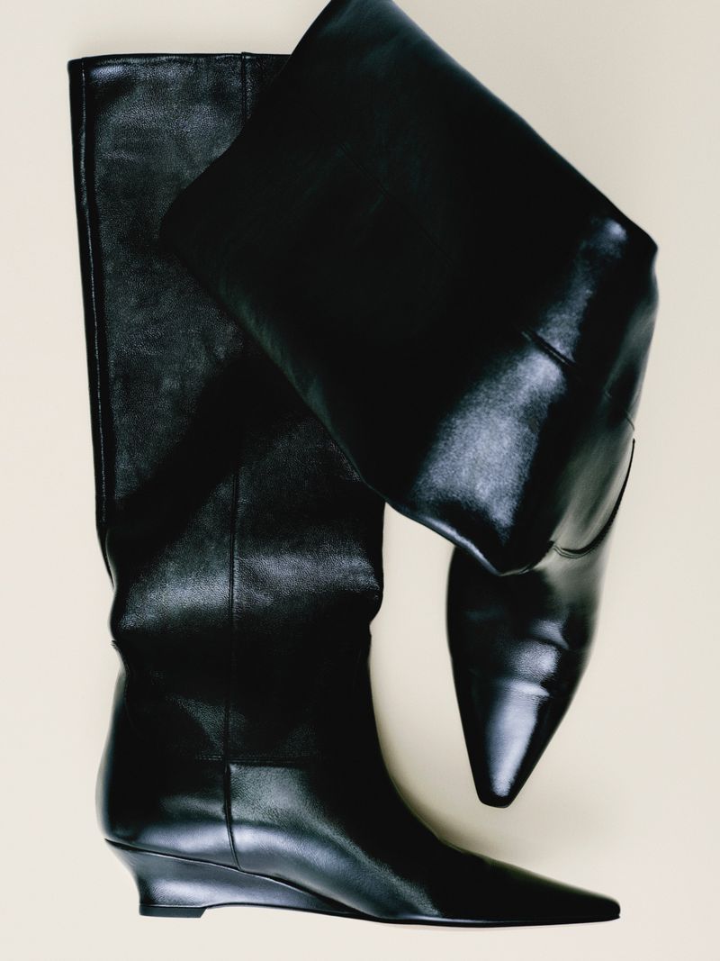 Elevated studio shot of a pair of black, knee-high leather boots with a slight wedge heel, against a neutral background.