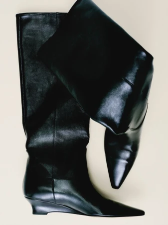 Elevated studio shot of a pair of black, knee-high leather boots with a slight wedge heel, against a neutral background.