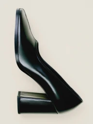 A black leather block-heel pump shoe positioned vertically against a plain off-white studio background.