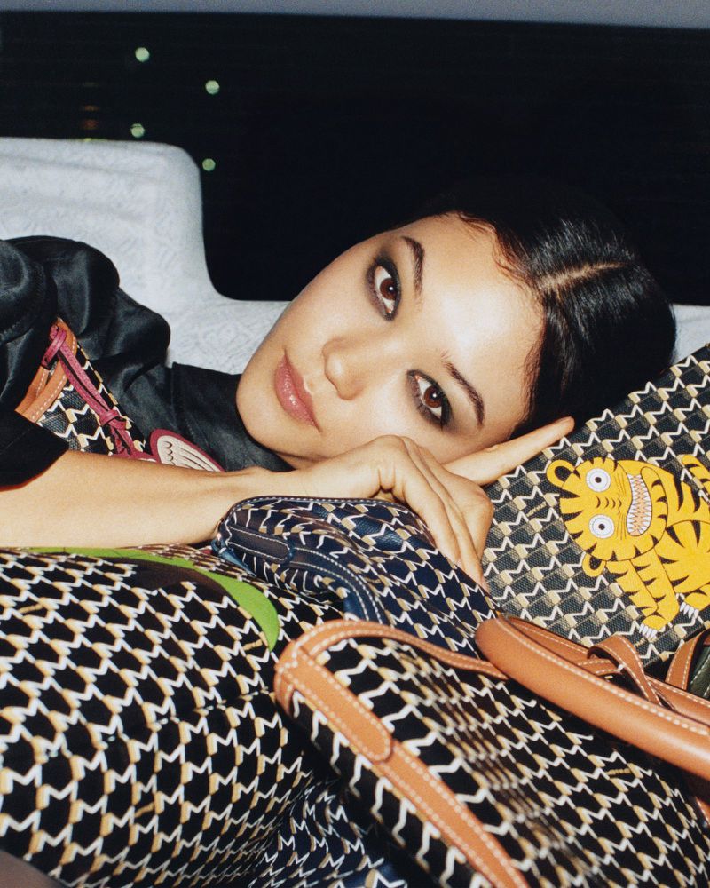 Model Mika Schneider reclining among patterned Moynat monogram bags featuring a graphic yellow tiger illustration.
