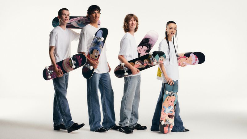 Group of five young adults holding skateboards in a studio setting, wearing casual attire and posing against a white backdrop. 