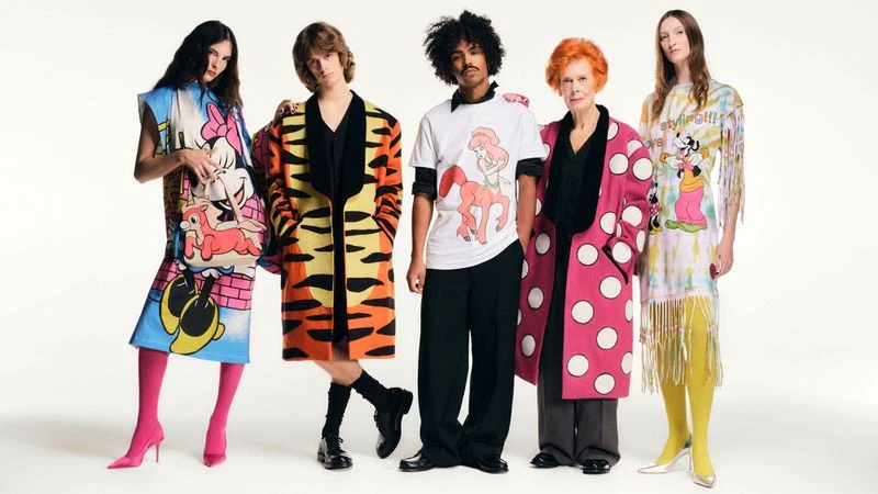 Five diverse fashion models showcase bold designer clothing with cartoon character prints in a studio setting against a white backdrop.