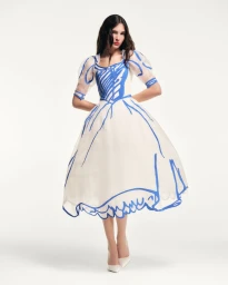 Enza Khoury poses in a white puff-sleeve dress with blue hand-drawn outlines and white pointed heels against a white studio background.