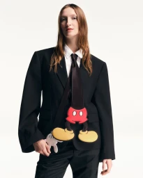 Model wearing a black tailored suit, white collared shirt, and a novelty Mickey Mouse tie against a white seamless background.