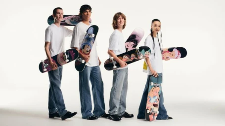 Four models in white t-shirts and baggy jeans hold Disney-illustrated skateboards against a seamless white studio background.