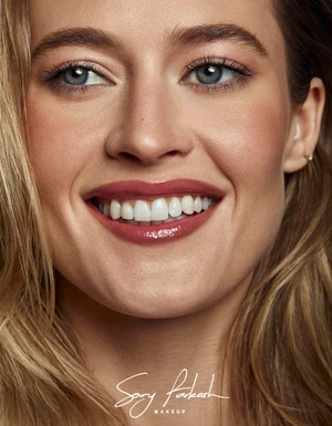 Close-up beauty portrait of model Hailey Carlson smiling with glossy rose lipstick and blonde hair.