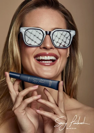 Hailey Carlson smiling in reflective sunglasses while holding a blue cosmetic tube for Sary Farkash Makeup shot by Yossi Michaeli.