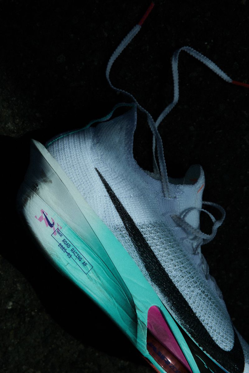 Close-up of a white Nike road racing shoe with a black swoosh logo, turquoise and pink accents, and a white lace on a dark surface.