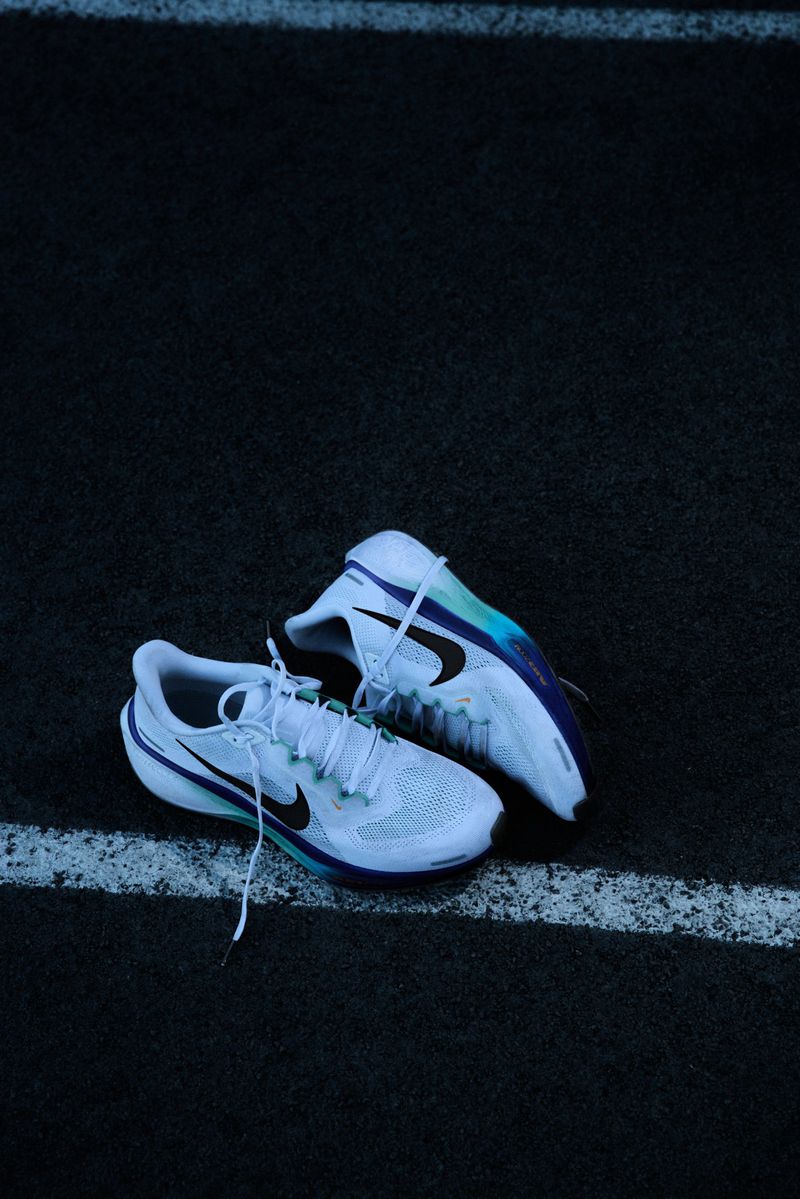 Pair of white Nike running shoes on a dark asphalt surface with a white stripe, athletic footwear, fitness, and sportswear concept.