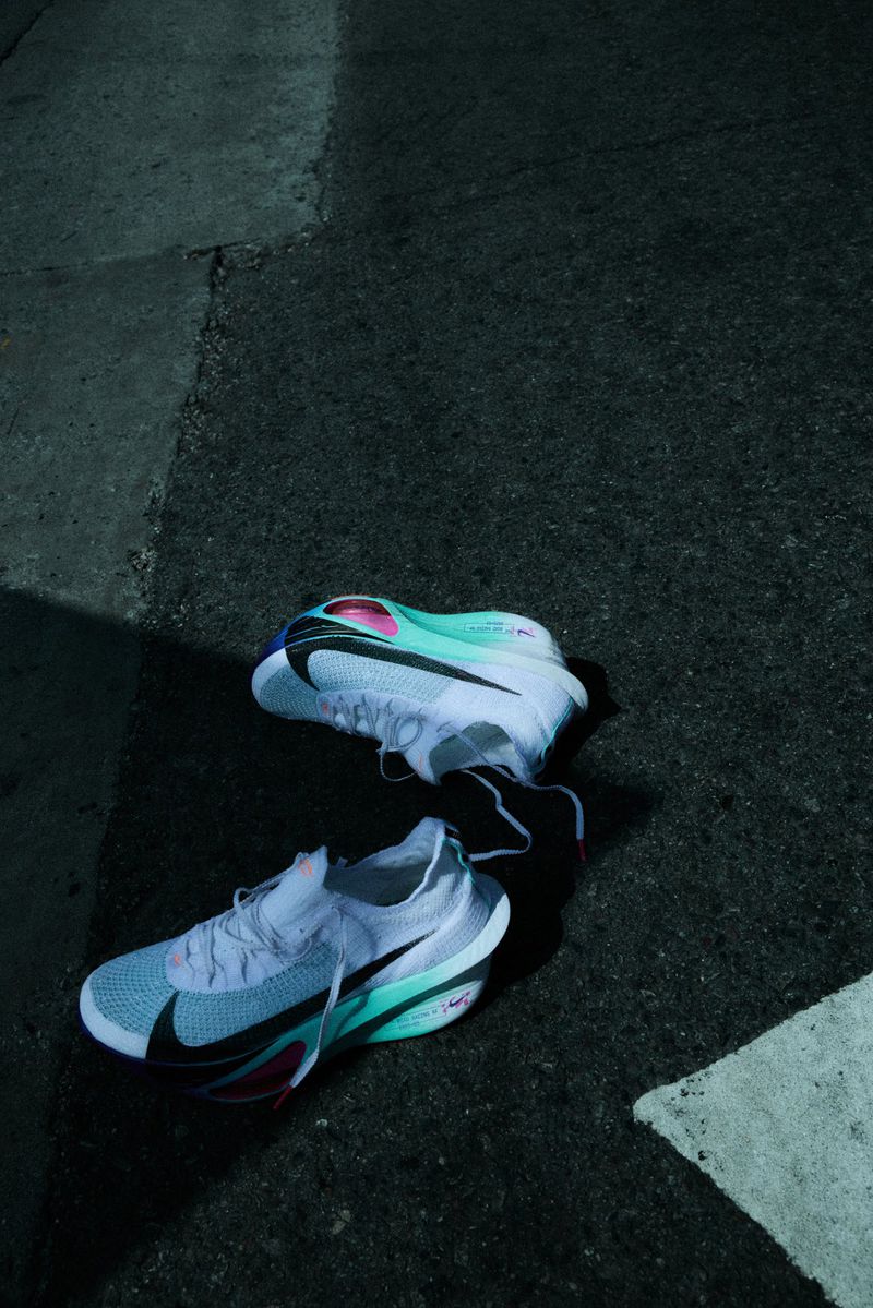 Two Nike running shoes on asphalt, in a close-up shot with turquoise and black accents, designed for athletic performance.