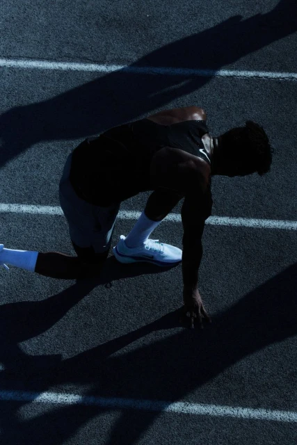 Athlete in starting position on running track, silhouetted against bright lane lines, showcasing determination and focus in fitness and sport.
