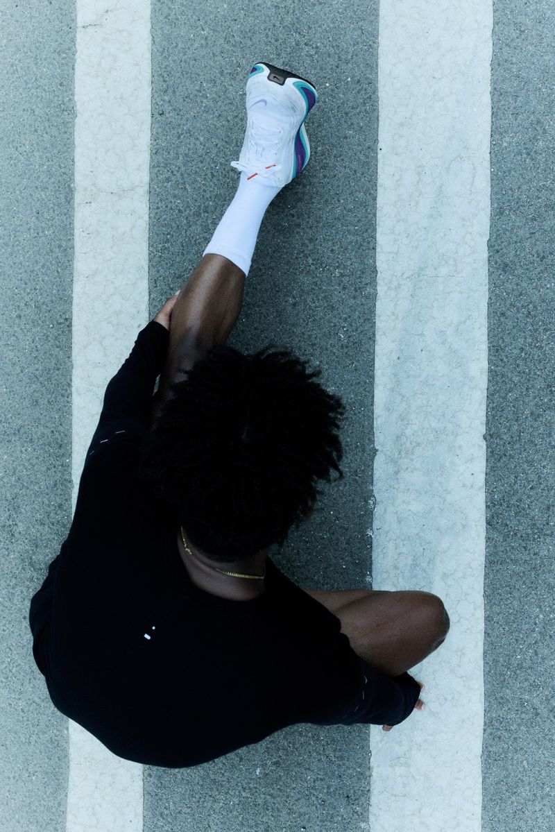Overhead shot of an adult stretching leg wearing white athletic shoe and sock, black workout top on a striped concrete surface.