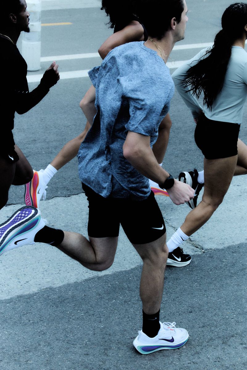 A group of adult runners, clad in athletic apparel and shoes, are captured in motion on a paved surface outdoors during daylight hours.