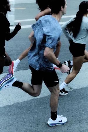 A group of adult runners, clad in athletic apparel and shoes, are captured in motion on a paved surface outdoors during daylight hours.