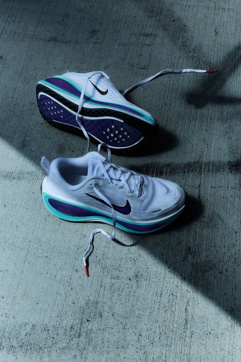 Elevated shot of two white Nike running shoes with black swooshes and purple and teal accents on a textured concrete surface.