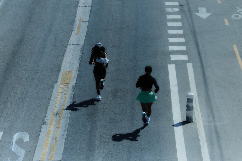 High-angle shot of two women running on a road marked with street lines and zebra crossing; fitness and urban lifestyle concept.